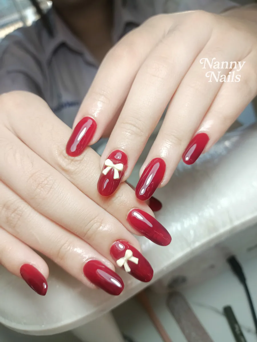 เล็บเจลสีแดงไวน์ ติดโบว์ขาว สีเข้มที่ต้องทาเบสรองพื้น ร้านทำเล็บนครพนม Nanny Nails