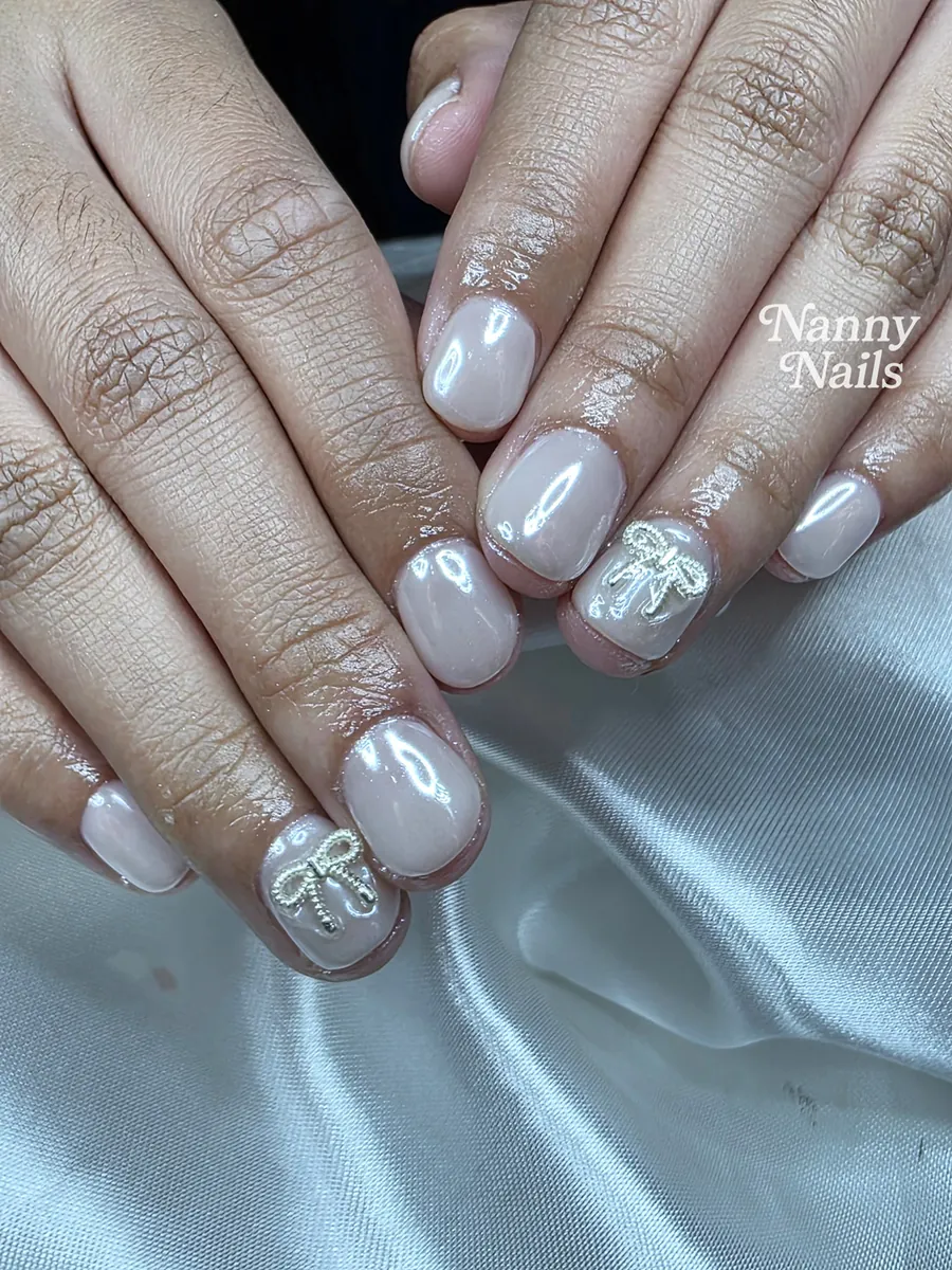Milky white gel nails with a silver bow charm on one nail per hand, Nanny Nails, nail salon in Nakhon Phanom