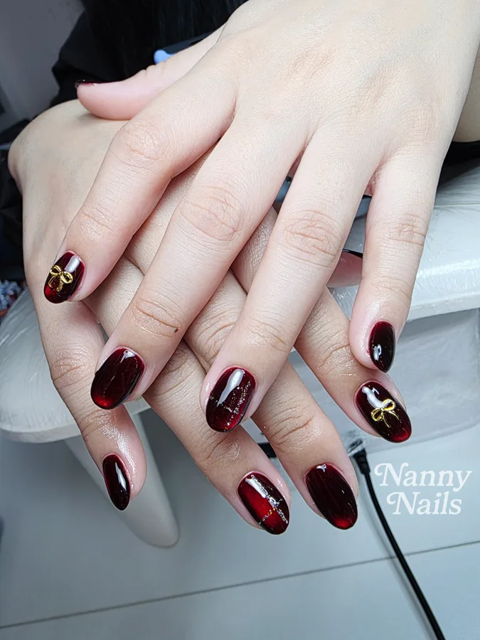 Burgundy cat eye nails with gold bows, Nanny Nails, nail salon in Nakhon Phanom
